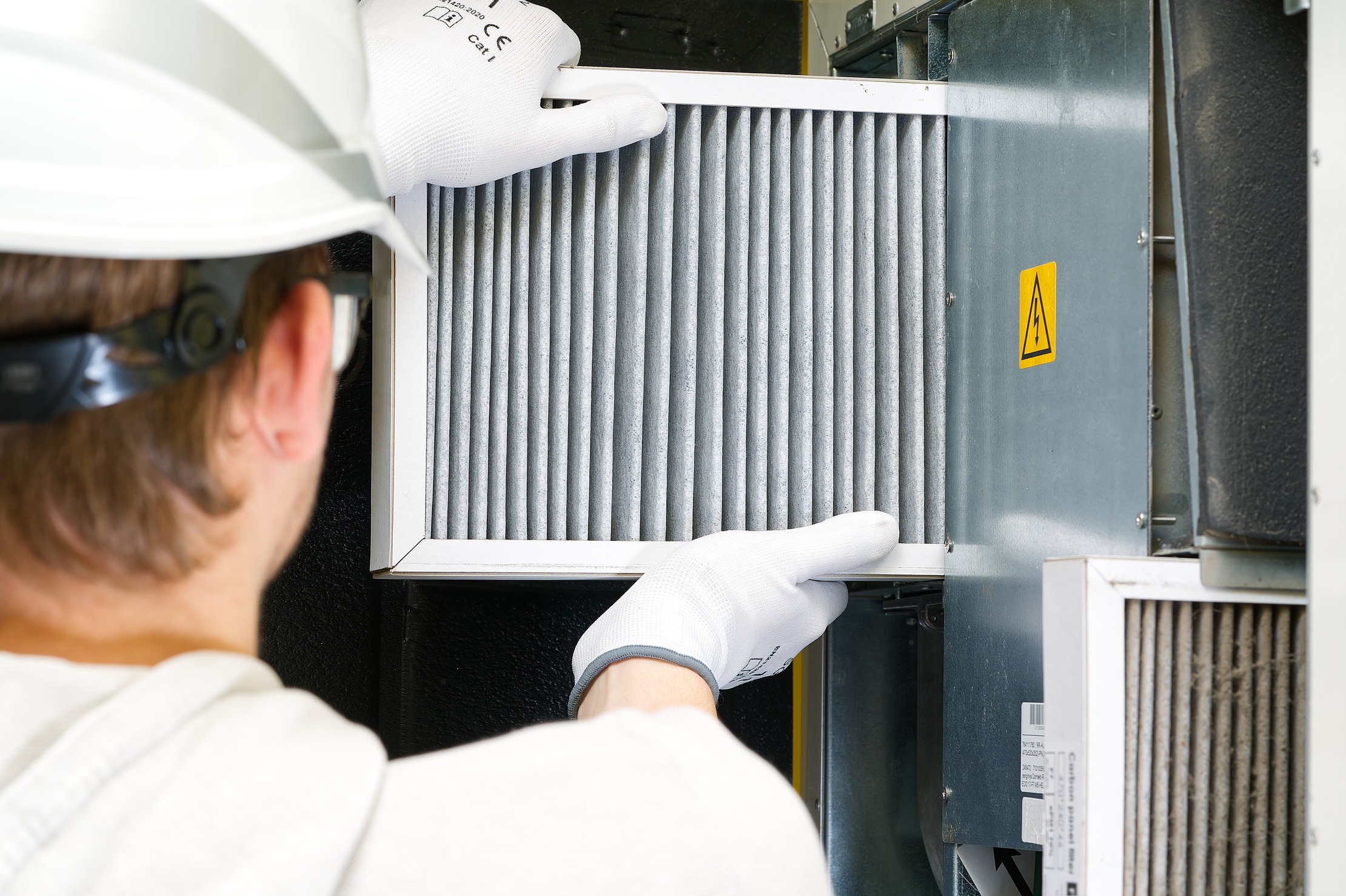 A technician wearing a safety helmet and gloves replaces an air filter in HVAC equipment, ensuring optimal performance and air quality.