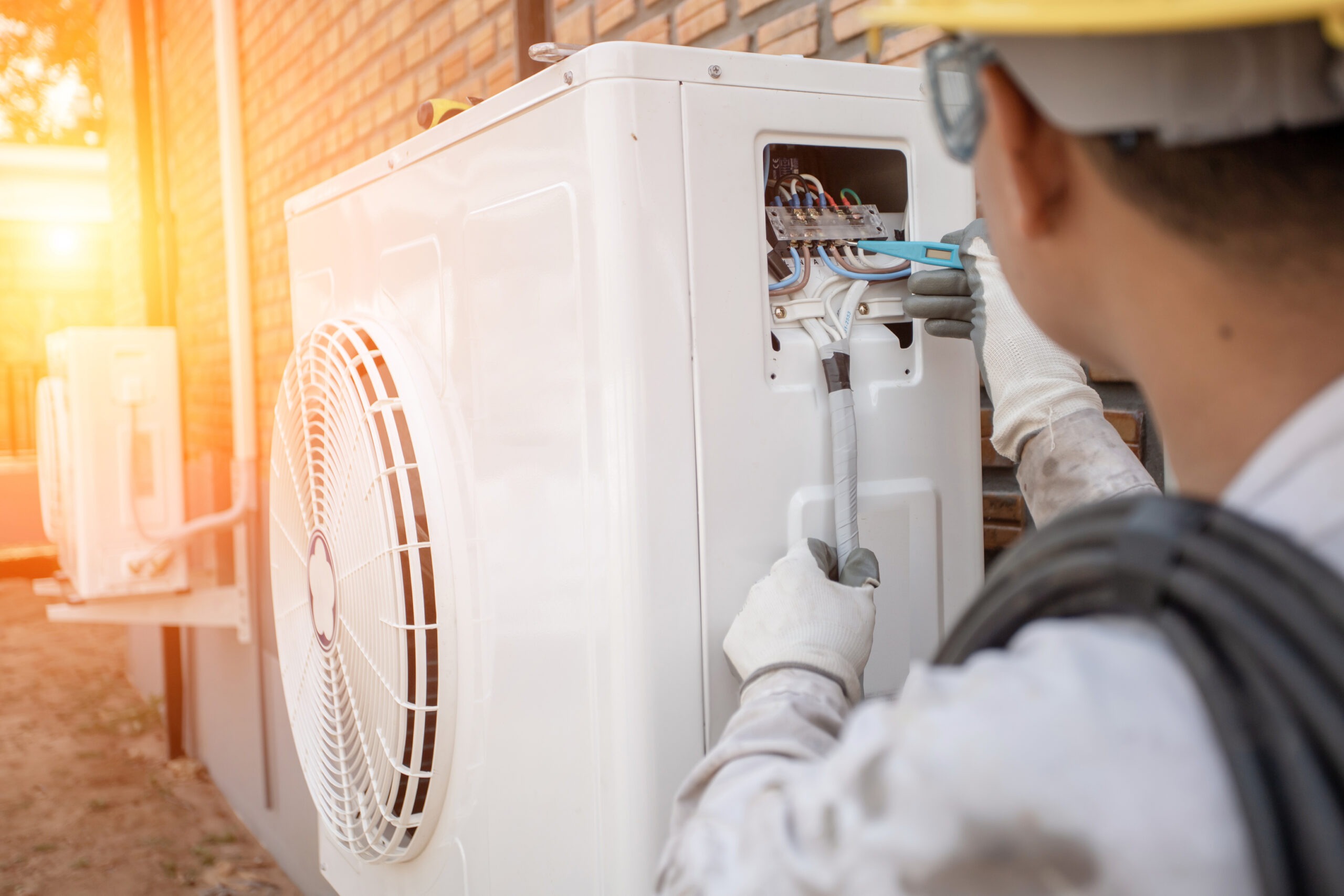 A technician in gloves repairs an outdoor air conditioning unit, focusing on electrical connections. The image illustrates HVAC service work.