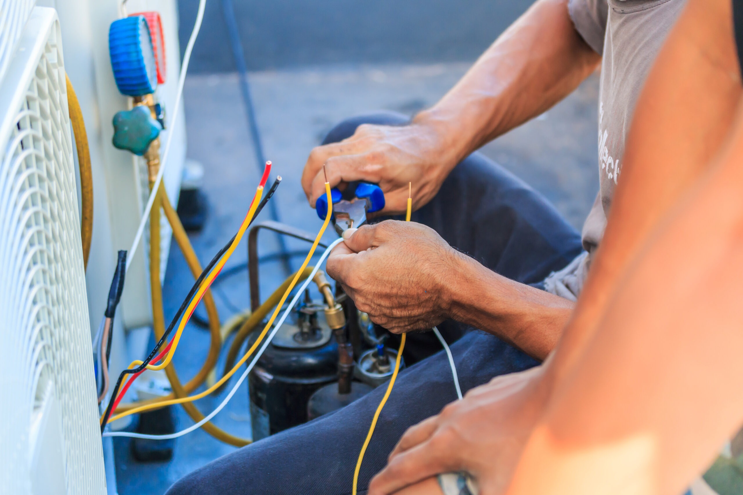 Technician repairing an air conditioning unit, focusing on connecting wires with tools, emphasizing hands-on work and technical skill.
