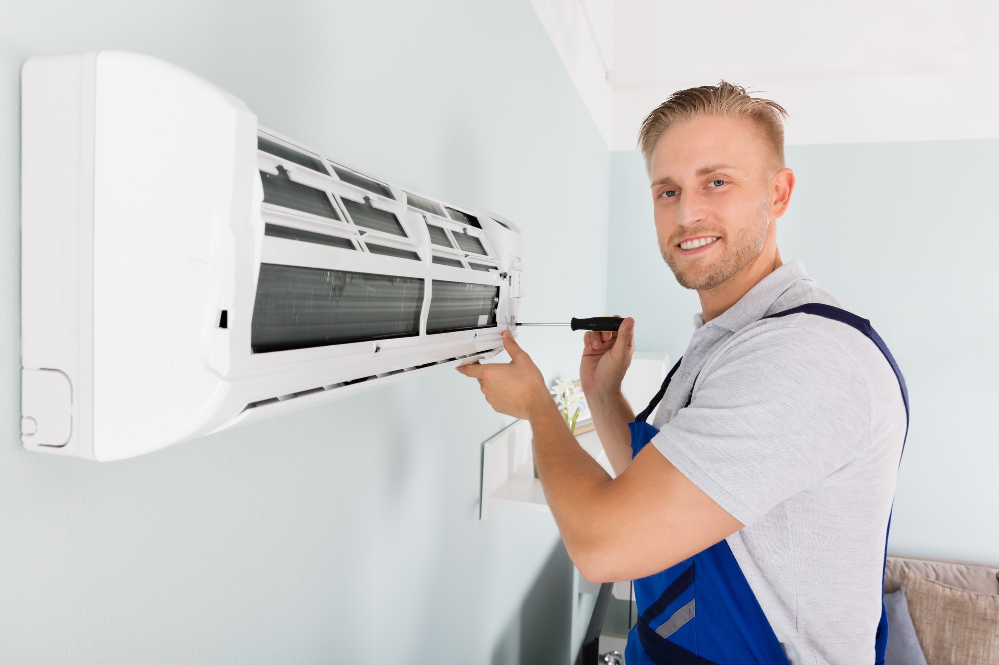 Young Male Technician Fixing Air Conditioner With Screwdriver