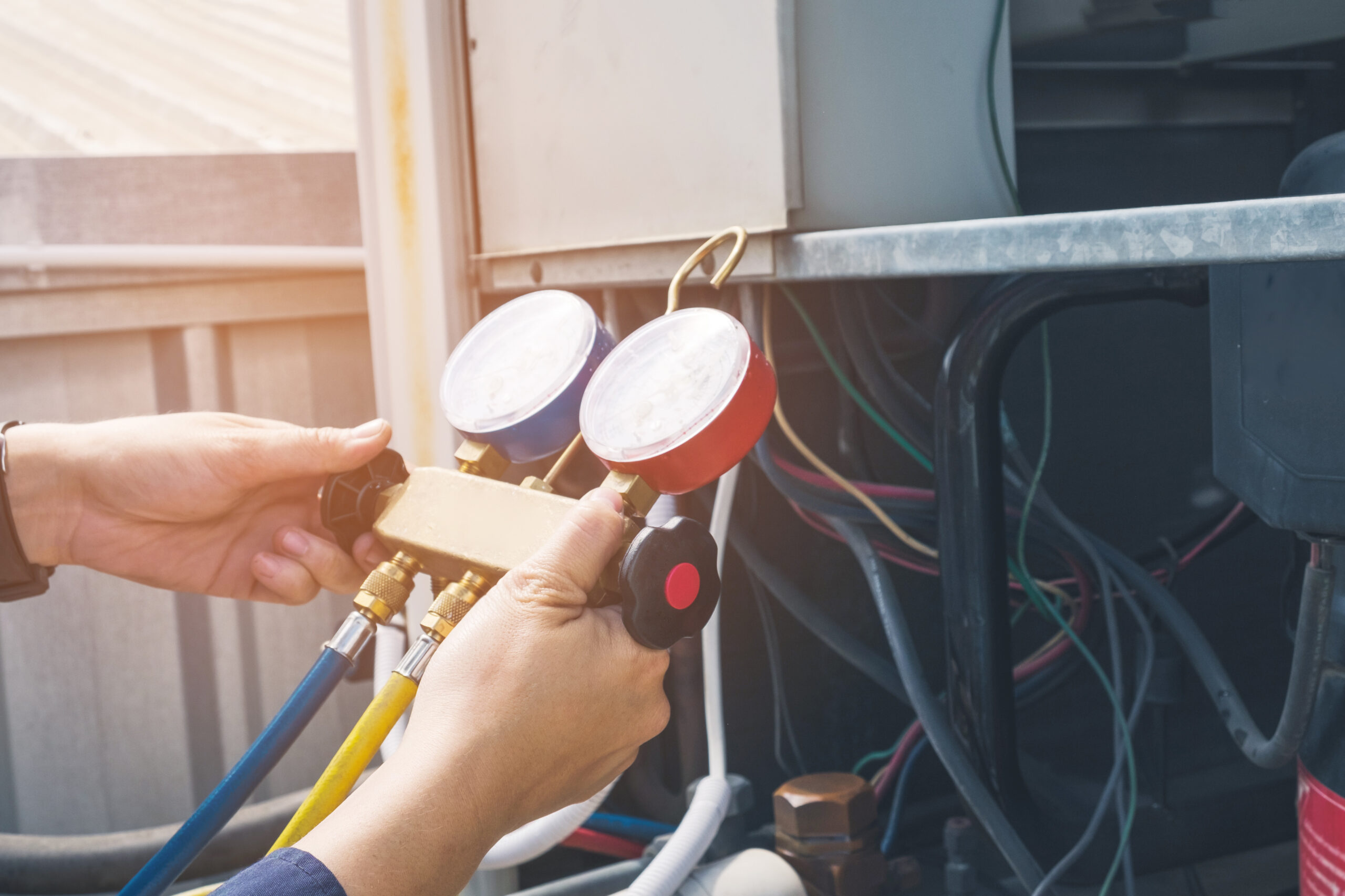 A technician holds HVAC pressure gauges, preparing to check connections on an air conditioning unit, illustrating routine maintenance.